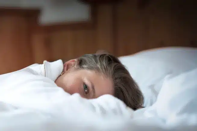 Model im Bett liegend auf dem Bett im Bademantel. Man erkennt nur Ihre Augen und Haare