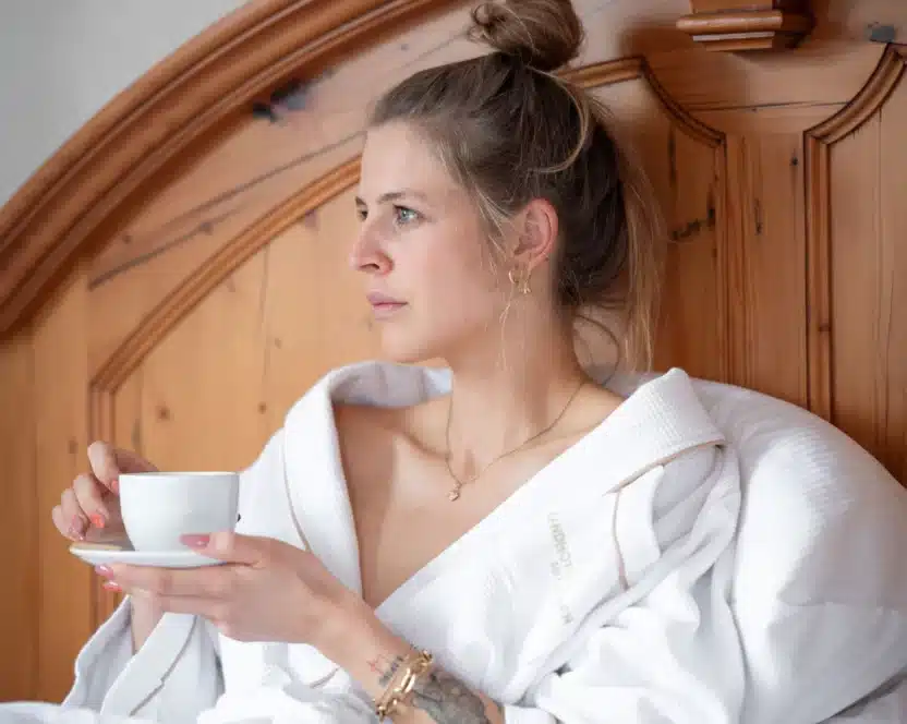 Junge Dame im Bademantel mit Tasse Kaffee im Bett