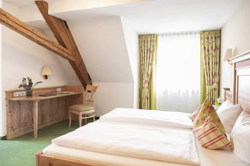 Zimmer 202: „Gemütliches Doppelzimmer mit Holzbalken, einem kleinen Schreibtisch und einem großen Fenster mit floralen Vorhängen im Landhotel 3Kronen.“